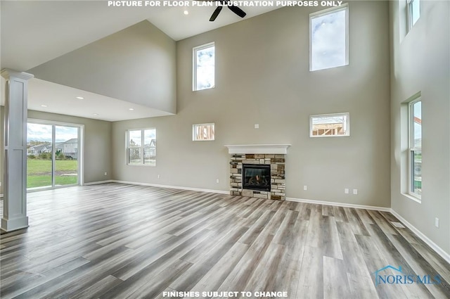 unfurnished living room featuring ceiling fan, a stone fireplace, a towering ceiling, and light wood-type flooring