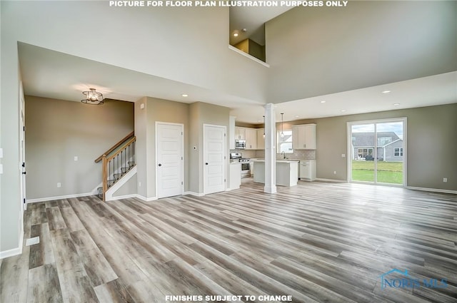 unfurnished living room featuring a towering ceiling, sink, and light hardwood / wood-style flooring