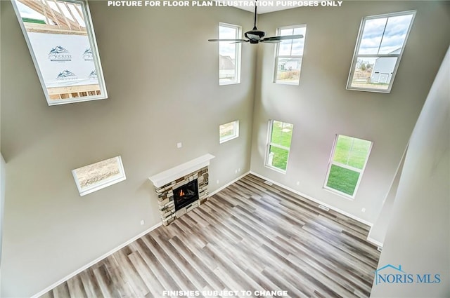 unfurnished living room featuring light hardwood / wood-style floors, a stone fireplace, and ceiling fan