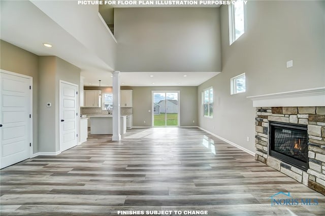 unfurnished living room with a stone fireplace, a towering ceiling, and light hardwood / wood-style flooring