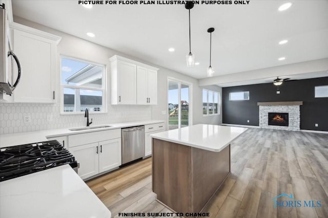 kitchen featuring dishwasher, sink, hanging light fixtures, a fireplace, and white cabinetry