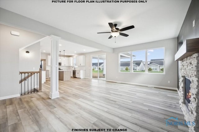 unfurnished living room with light wood-type flooring, a stone fireplace, and ceiling fan