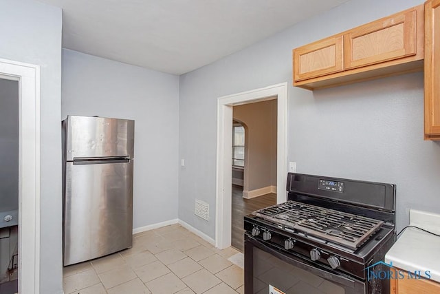 kitchen featuring stainless steel fridge, black range with gas stovetop, light tile patterned floors, and light brown cabinetry