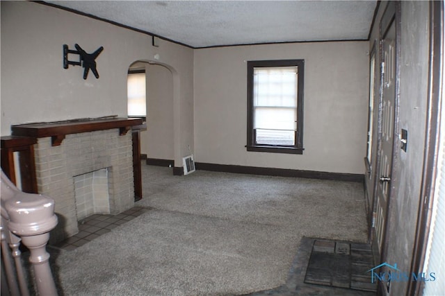 unfurnished living room with a fireplace, a textured ceiling, arched walkways, carpet flooring, and baseboards