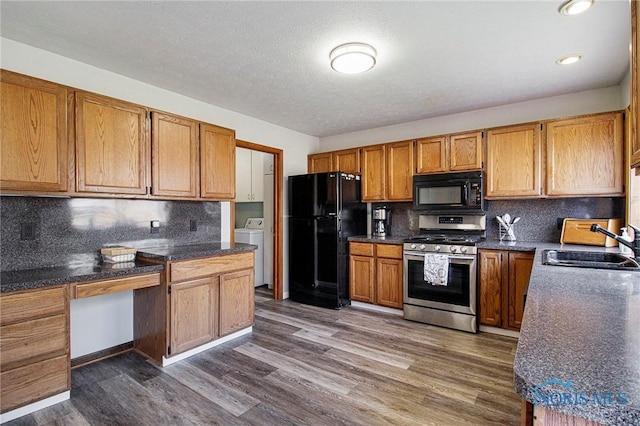 kitchen featuring black appliances, sink, dark hardwood / wood-style floors, tasteful backsplash, and washer / dryer