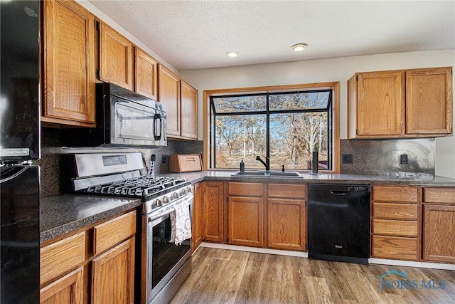 kitchen featuring black appliances, sink, light wood-type flooring, a textured ceiling, and tasteful backsplash