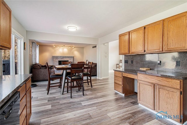 kitchen with tasteful backsplash, a fireplace, dishwasher, and light hardwood / wood-style flooring