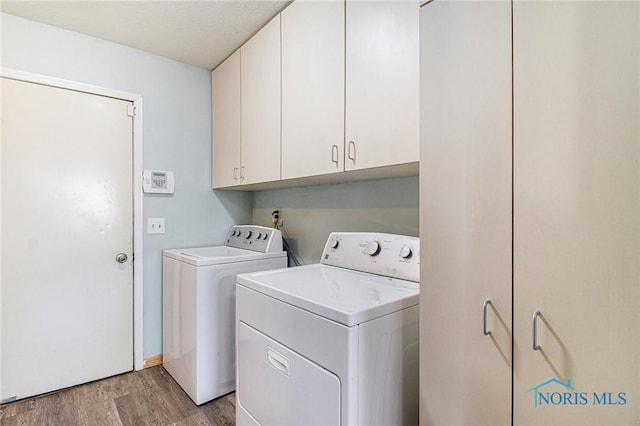 washroom featuring washing machine and clothes dryer, light hardwood / wood-style flooring, and cabinets