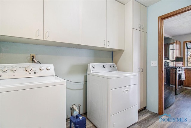 laundry area featuring washer and dryer, a textured ceiling, light wood-type flooring, and cabinets