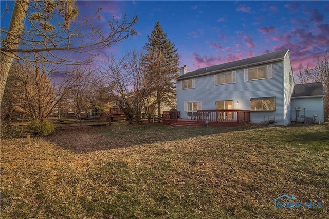 back house at dusk featuring a lawn and a wooden deck