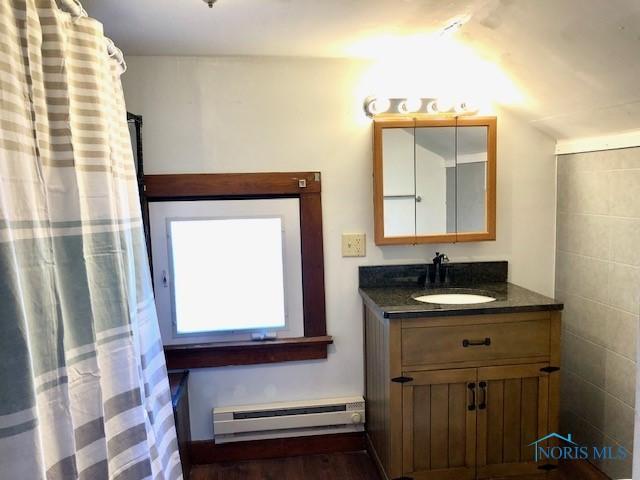 bathroom with hardwood / wood-style flooring, vanity, tile walls, and a baseboard heating unit