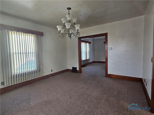 unfurnished room with a wealth of natural light, dark colored carpet, and a notable chandelier