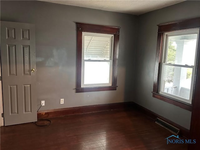 unfurnished room with a textured ceiling, a healthy amount of sunlight, and dark hardwood / wood-style floors