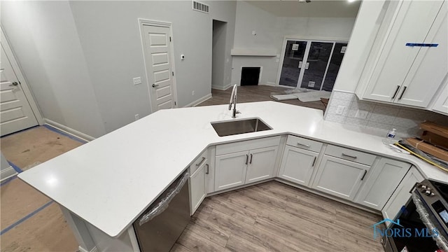 kitchen with sink, light hardwood / wood-style flooring, stainless steel dishwasher, and white cabinets