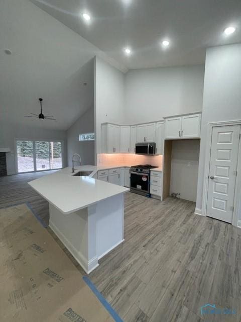 kitchen featuring stainless steel microwave, open floor plan, high vaulted ceiling, a sink, and gas stove