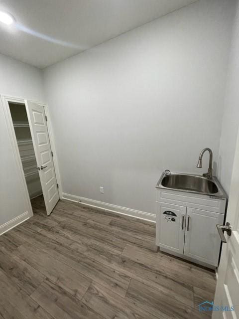 unfurnished bedroom featuring wood finished floors, a sink, and baseboards