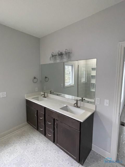 full bathroom featuring a tile shower, double vanity, a sink, and baseboards