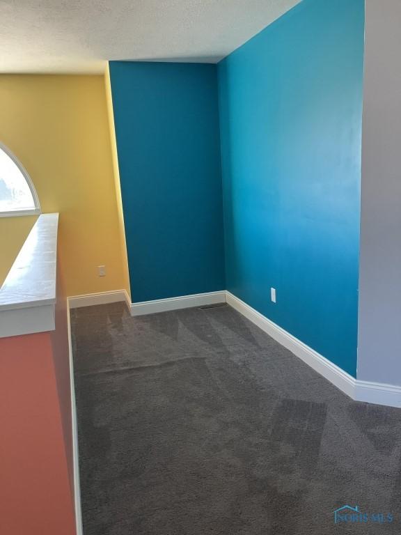 spare room featuring dark colored carpet and a textured ceiling