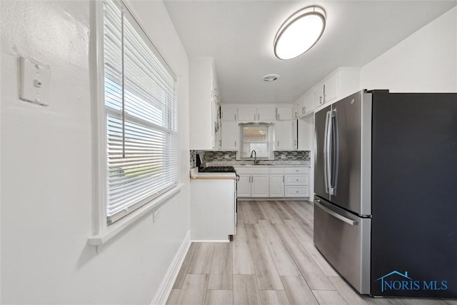 kitchen featuring tasteful backsplash, sink, light hardwood / wood-style floors, white cabinetry, and stainless steel refrigerator