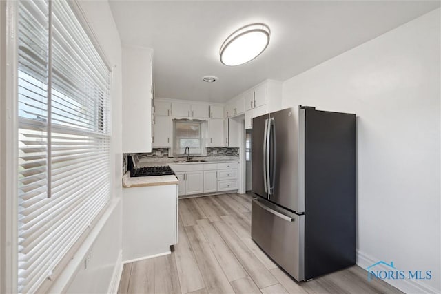 kitchen with sink, appliances with stainless steel finishes, decorative backsplash, white cabinets, and light wood-type flooring