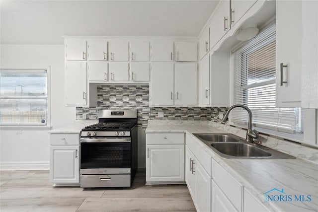 kitchen with backsplash, gas range, sink, and white cabinets