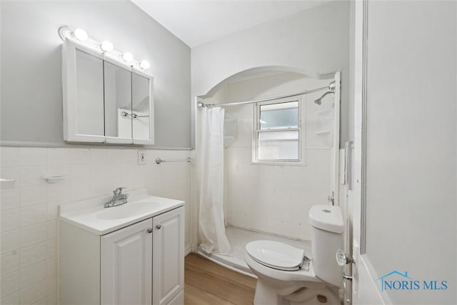 bathroom with hardwood / wood-style floors, vanity, a shower with curtain, toilet, and tile walls