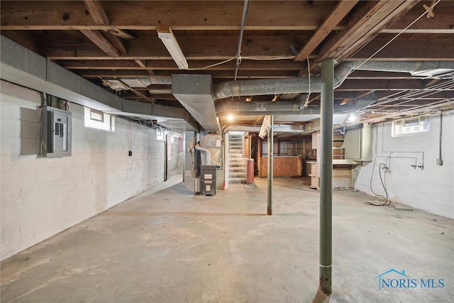 basement featuring electric panel, a wealth of natural light, and heating unit