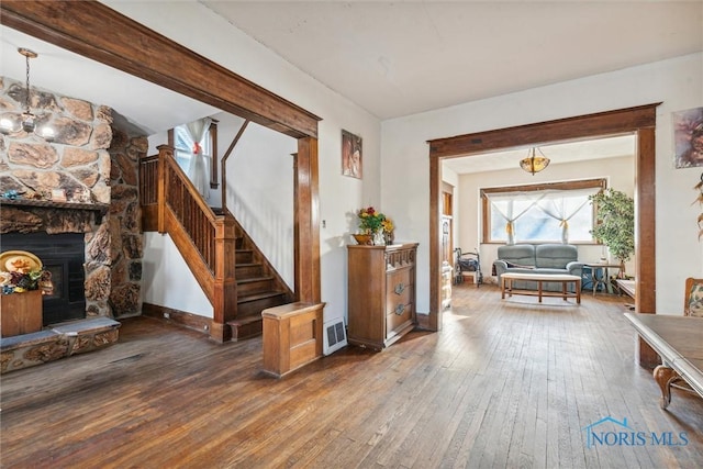 foyer with a stone fireplace, beamed ceiling, dark hardwood / wood-style floors, and a notable chandelier