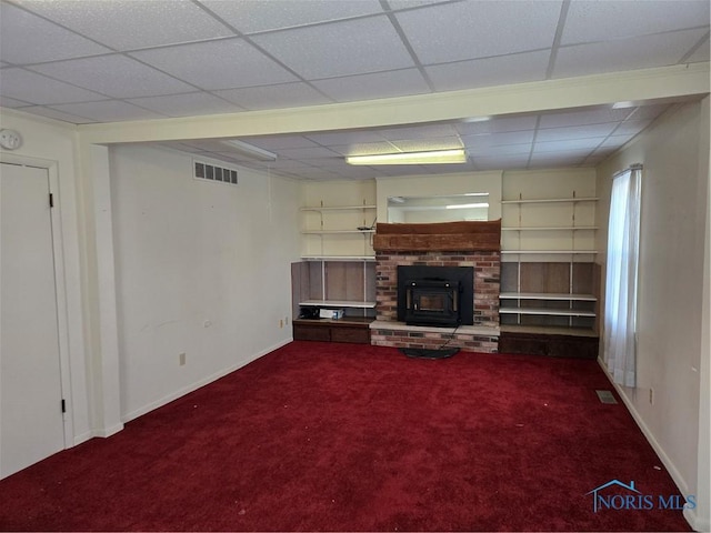 unfurnished living room featuring a wood stove, a paneled ceiling, and carpet floors