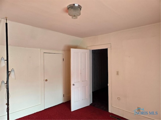 unfurnished bedroom featuring dark colored carpet, a closet, and lofted ceiling