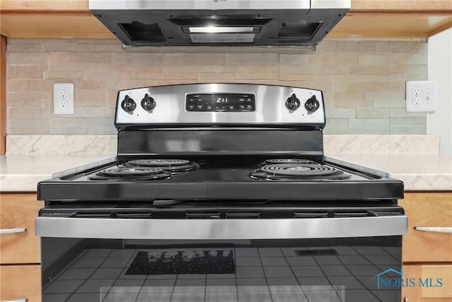 kitchen with stainless steel range, backsplash, tile patterned floors, and exhaust hood