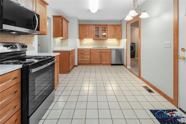 kitchen featuring tasteful backsplash, stainless steel appliances, sink, washer / dryer, and hanging light fixtures