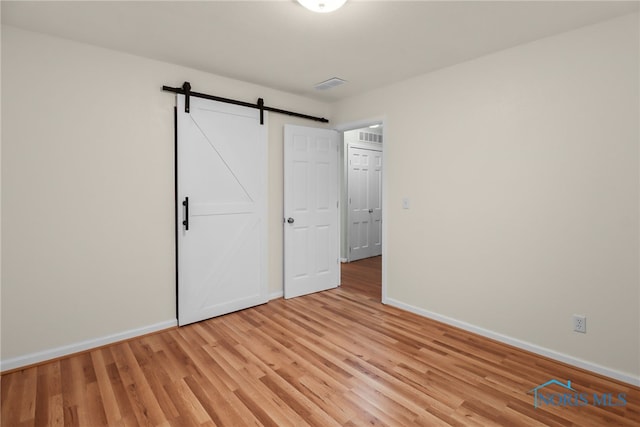 unfurnished bedroom featuring a barn door and light hardwood / wood-style flooring