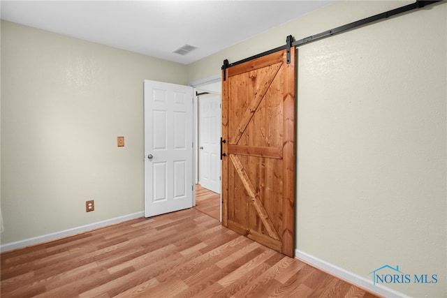 unfurnished bedroom with a barn door and light wood-type flooring