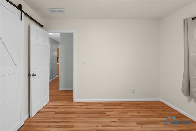 unfurnished bedroom featuring a barn door and light hardwood / wood-style flooring