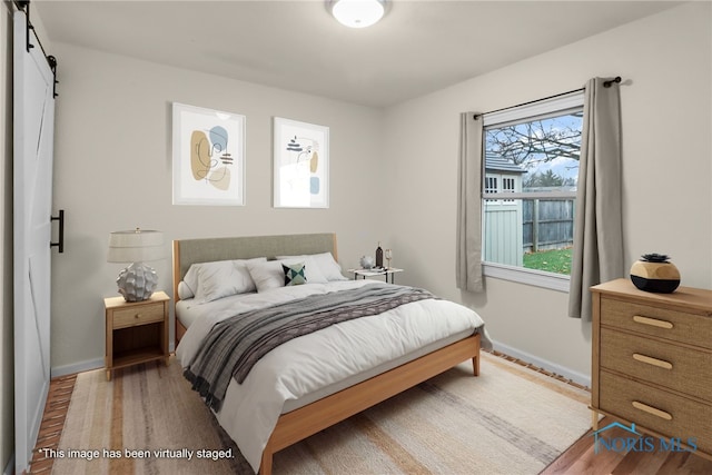 bedroom with wood-type flooring, a barn door, and multiple windows