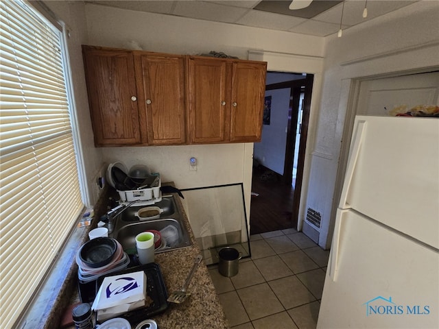 kitchen featuring sink, a drop ceiling, white refrigerator, dark stone counters, and light tile patterned floors