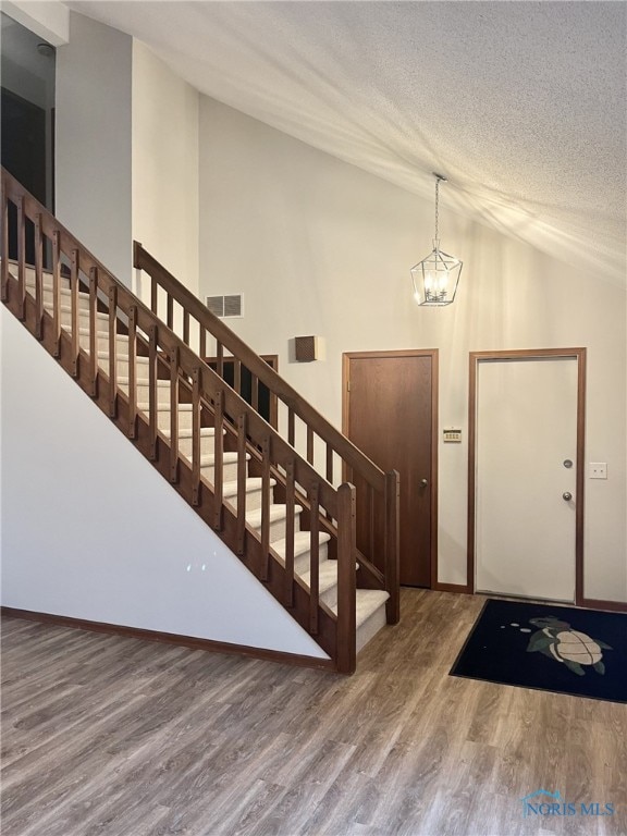 entryway featuring hardwood / wood-style floors, a notable chandelier, lofted ceiling, and a textured ceiling