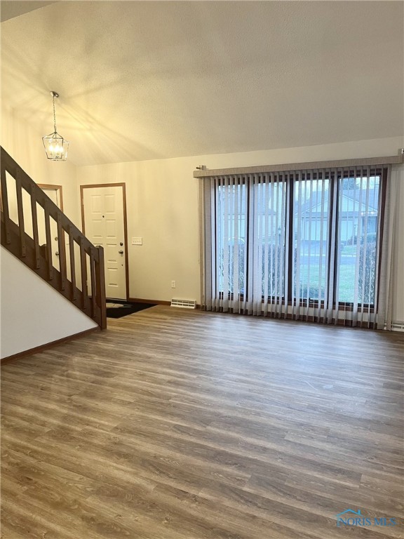 unfurnished living room featuring a notable chandelier, dark hardwood / wood-style floors, a wealth of natural light, and vaulted ceiling