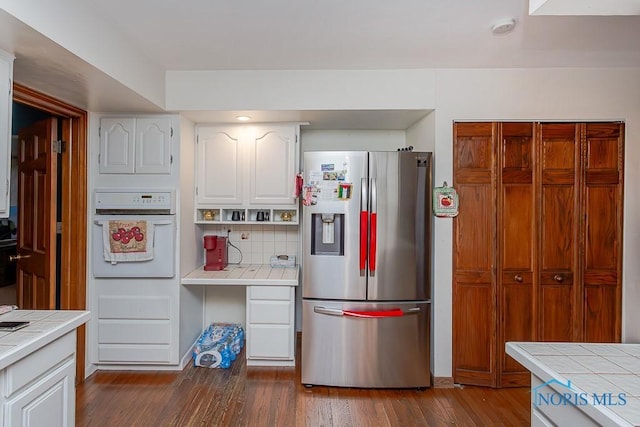 kitchen featuring stainless steel fridge, white oven, dark hardwood / wood-style floors, and tile counters