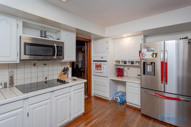 kitchen with white cabinets, wood-type flooring, appliances with stainless steel finishes, and tile countertops