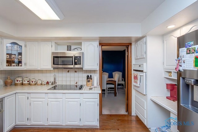 kitchen with decorative backsplash, stainless steel appliances, white cabinetry, and hardwood / wood-style flooring