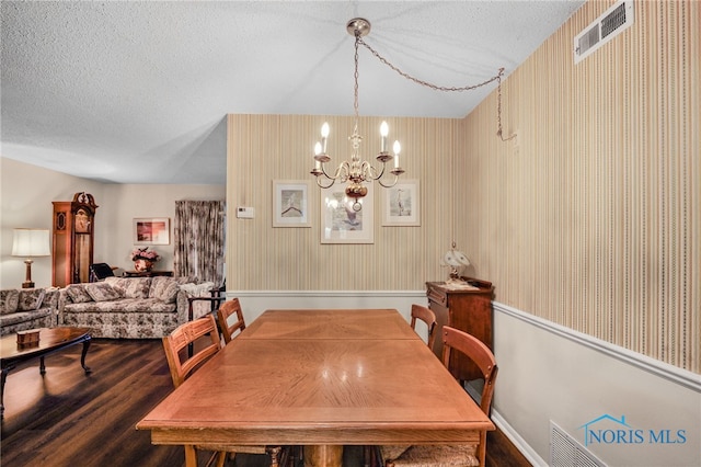 dining area with dark hardwood / wood-style flooring, a textured ceiling, and an inviting chandelier