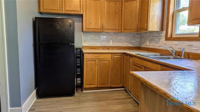 kitchen with black refrigerator, backsplash, light hardwood / wood-style flooring, and sink