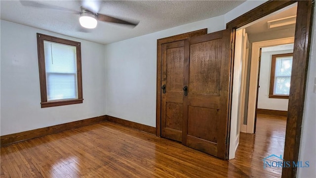 unfurnished bedroom with ceiling fan, wood-type flooring, a textured ceiling, and a closet