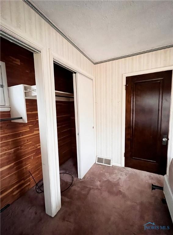 unfurnished bedroom with dark colored carpet, wood walls, a textured ceiling, and a closet