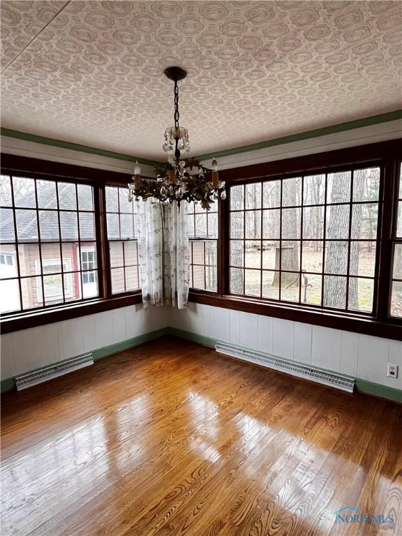 unfurnished dining area with baseboard heating, plenty of natural light, wood-type flooring, and a notable chandelier