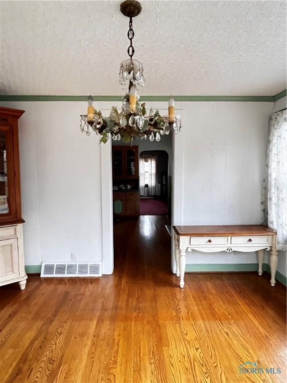 unfurnished dining area featuring crown molding, a textured ceiling, and hardwood / wood-style flooring