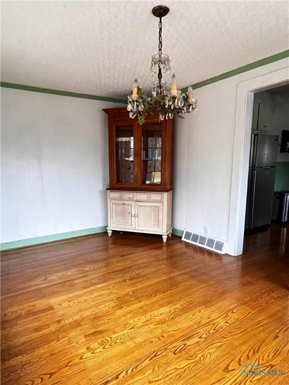 unfurnished dining area featuring a notable chandelier, crown molding, wood-type flooring, and a textured ceiling