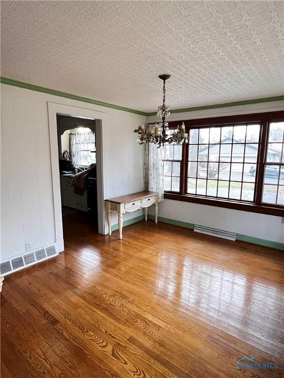 unfurnished dining area with hardwood / wood-style floors, a textured ceiling, and an inviting chandelier